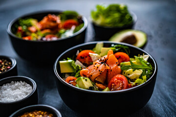 Salmon salad - smoked salmon with avocado and mix of vegetables on black wooden table
