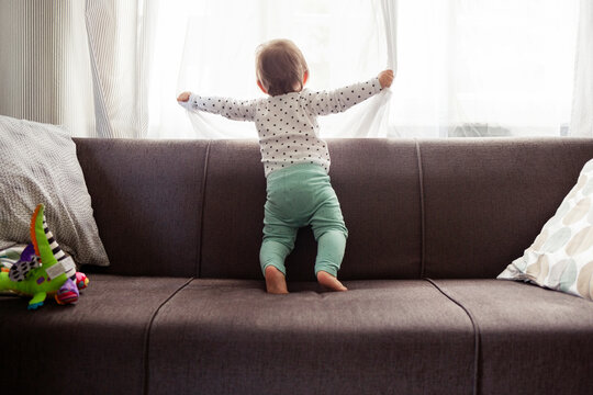 Baby girl looking through window while standing on sofa at home