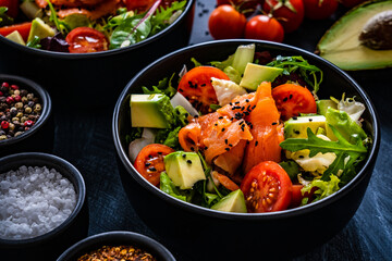 Salmon salad - smoked salmon with avocado and mix of vegetables on black wooden table
