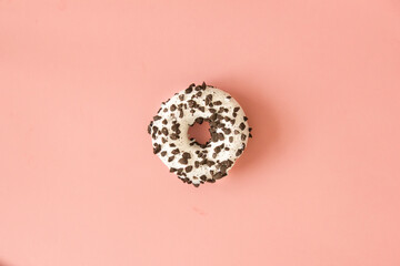 Round donut with chocolate crumbs and white icing on a pink background.