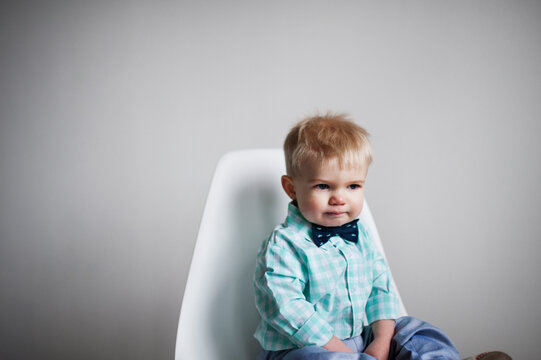 Sad baby boy sitting on chair against white wall at home