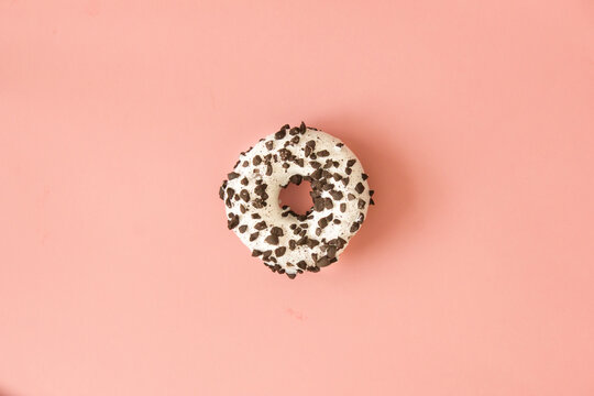 Round Donut With Chocolate Crumbs And White Icing On A Pink Background.