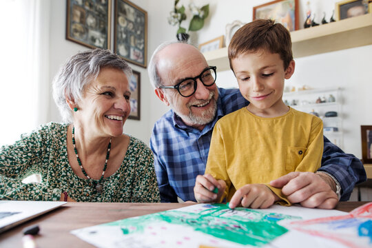 Happy grandparents looking at grandson making drawing at home