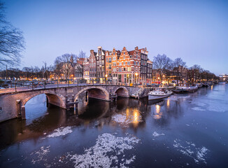 Frozen Amsterdam canals at the Brouwersgracht with famous historic architecture, snow and ice during blue hour with a clear sky
