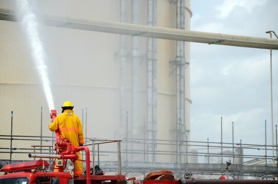 Fireman use fire hose water spray from fire truck to the Large chemical tank in part of fire drill or emergency drill training in tank farm at onshore, oil and gas or chemical factory.