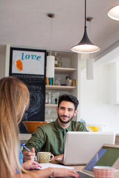 Smiling man looking at woman while using laptop at home