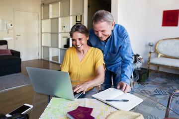 Happy senior couple using laptop while planning vacation at home