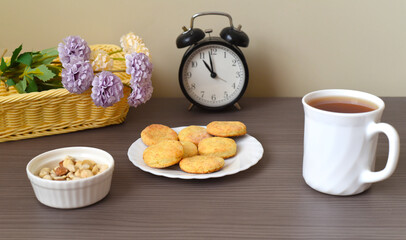 Round homemade curd cookies on a plate next to cup of tea and basket with flowers