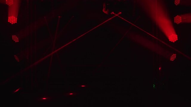 Bright red laser lights and spotlights dynamically rotate and move over dark stage. Shining empty stage for holiday show, awards ceremony or advertisement. Night laser show of holograms.