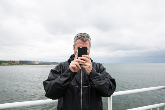 Man photographing while standing by railing against sea