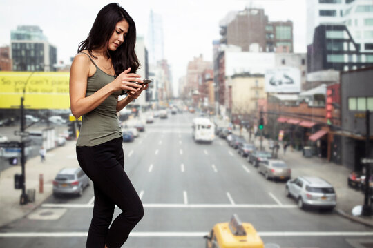 Young woman using smart phone by glass window with city street in background