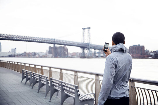 Rear view of male athlete photographing Williamsburg Bridge