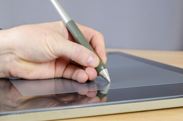 A designer's hand drawing with a special pen on the screen of a graphics tablet.