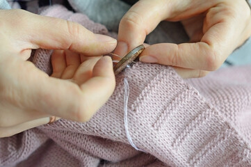 female workers' hands sew a wooden button to a jacket. close-up.