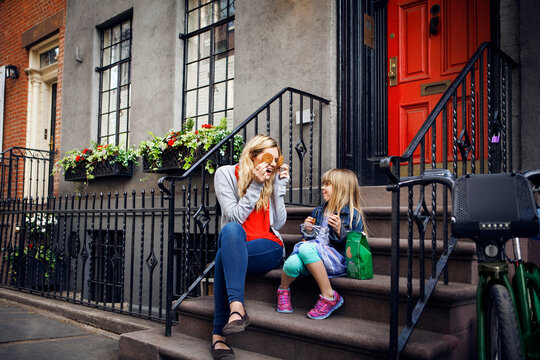 Playful mother holding cookies in front of eyes while sitting with daughter on steps