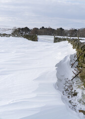 Snow drifts against a dry stone wall