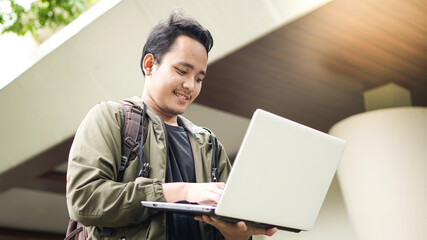smiling Asian man wearing a backpack with a laptop