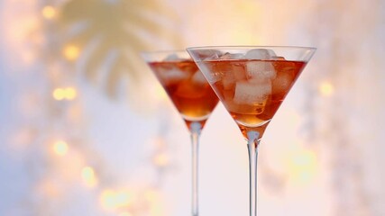 two glasses of red summer cocktail with ice cubes close up, defocused  festive lights in background