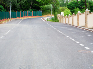 Obraz premium Freshly laid asphalt on the road with markings and fences along and green trees