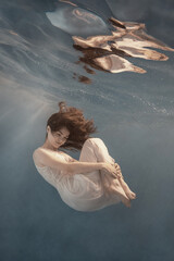 A girl in a white dress posing and somersaulting under water as if flying in zero gravity
