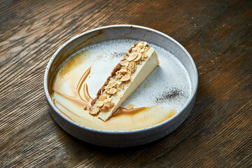 Classic slice of cheesecake with almonds and caramel sauce, served in a white plate on a wooden background. Restaurant food. Appetizing dessert