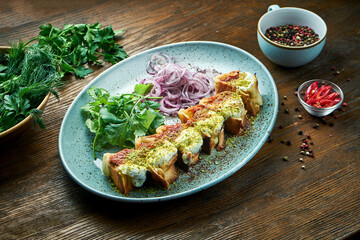 A classic Turkish dish is sliced shawarma with chicken kebab topped with red and white pistachio sauce, served in a blue plate on a wooden background. Restaurant food