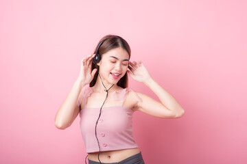 Happy smiling young asia woman with headphones enjoying listens to music over pink background