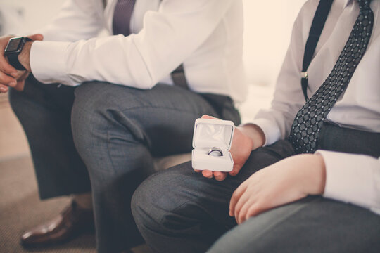 Midsection of bridegroom sitting by pageboy holding wedding ring while sitting on bed at home