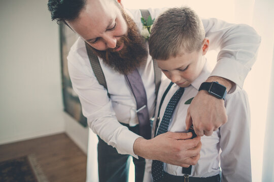 Bridegroom assisting pageboy in getting dressed at home