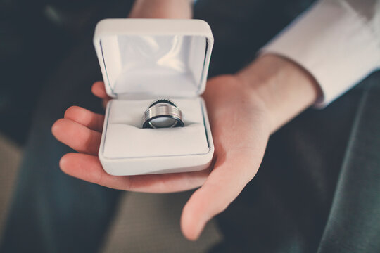 Cropped hand of pageboy holding wedding rings box while sitting with bridegroom at home