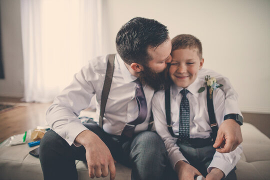 Happy bridegroom kissing pageboy while sitting on bed at home