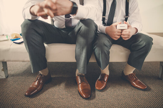 Low section of bridegroom with pageboy holding wedding ring box while sitting on bed at home