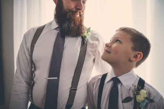 Smiling bridegroom and pageboy looking at each other while standing against curtain