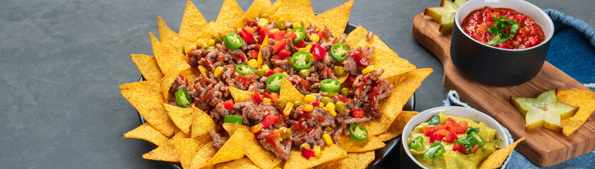 Hispanic mexican food, nachos with meat, corn and halapenjo on dark background