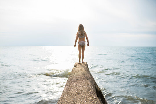 Rear view of girl standing on jetty at beach against sky