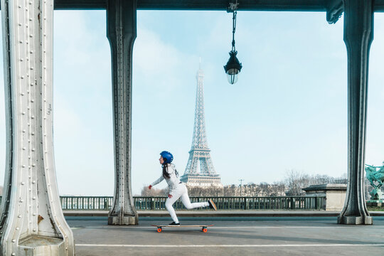 Side view of woman skateboarding under bridge against Eiffel Tower