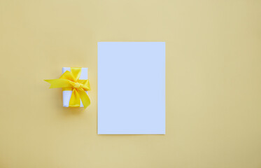 White invitation card mockup with small present box on yellow background
