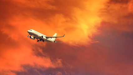 Zoom photo of passenger airplane taking off at sunset with beautiful orange sky and clouds