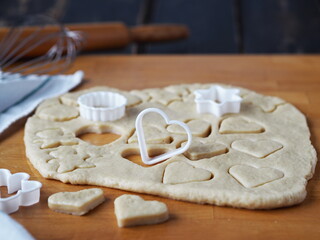 Confectionery background.Raw shortbread cookies cut from a layer of dough with cookie cutters on a kitchen board on a dark wooden table.