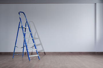 A dirty blue metal stepladder against a newly painted gray wall in a new building. The concept of professional renovation. Copy space.
