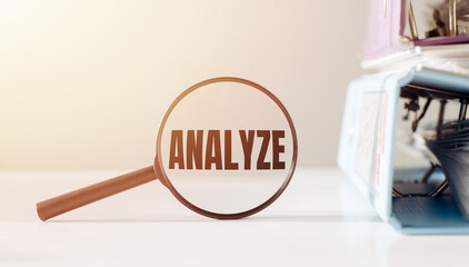 Magnifying glass with the word ANALYZE on office table.