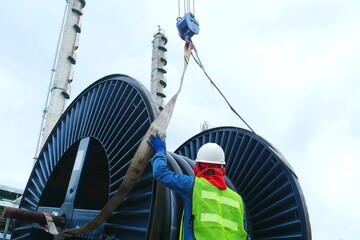 Worker or rigger during high risk and put on safety helmet commencing crane, boom truck is lifting big steel cable drum by using hand signal which meant crane is up in construction chemical site