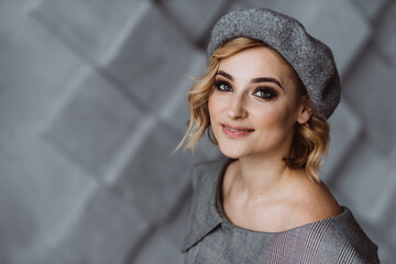 Portrait of a beautiful blonde woman with smoky eye makeup in a gray beret. Soft selective focus.