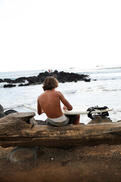 a surfer waxes his board before getting in the water near Hanga Roa