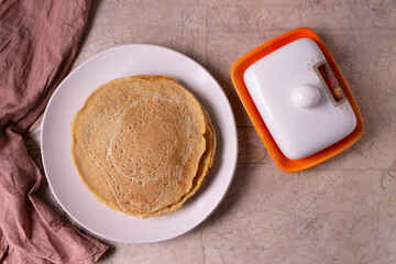 Oatmeal pancakes with on a round plate and butter dish on a beige background.