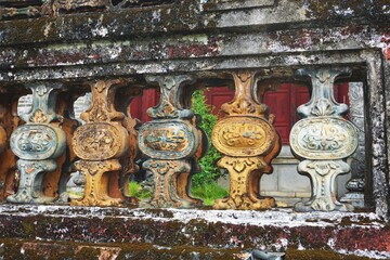 Glazed ceramic ornamental balusters set in ancient moss-covered fence in Southeast Asia
