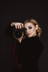 Beautiful stylish woman photographer in a black outfit with a camera in her hands. Soft selective focus.