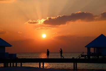 sunset on the wooden pier at a Maldives island with people silhouette
