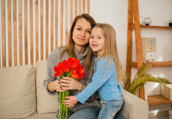 mom and daughter are sitting on the couch with a bouquet of red tulips in the room. Mother's Day