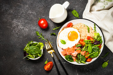 Savory breakfast. Oatmeal porrige with salted salmon, egg and fresh salad. Top view on black table.